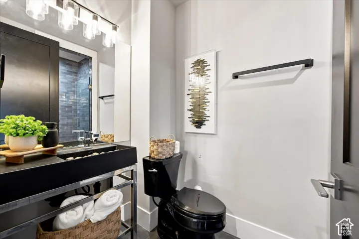 Vanity with integrated basin sink, black toilet, floor-to-ceiling mirror, and wall-mounted light fixture