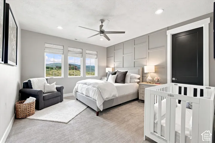 Accent wall with decorative paneling, recessed lighting, ceiling fan with light fixture, three windows with roman shades, and a dark panel door with white trim