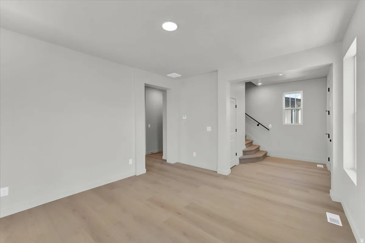 Wood-finish flooring, recessed lighting, neutral wall tones, and a carpeted staircase with a dark handrail