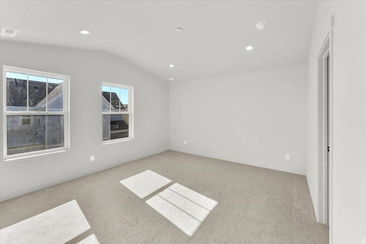Neutral wall color, recessed ceiling lighting, two double-hung windows, and light-colored carpet flooring