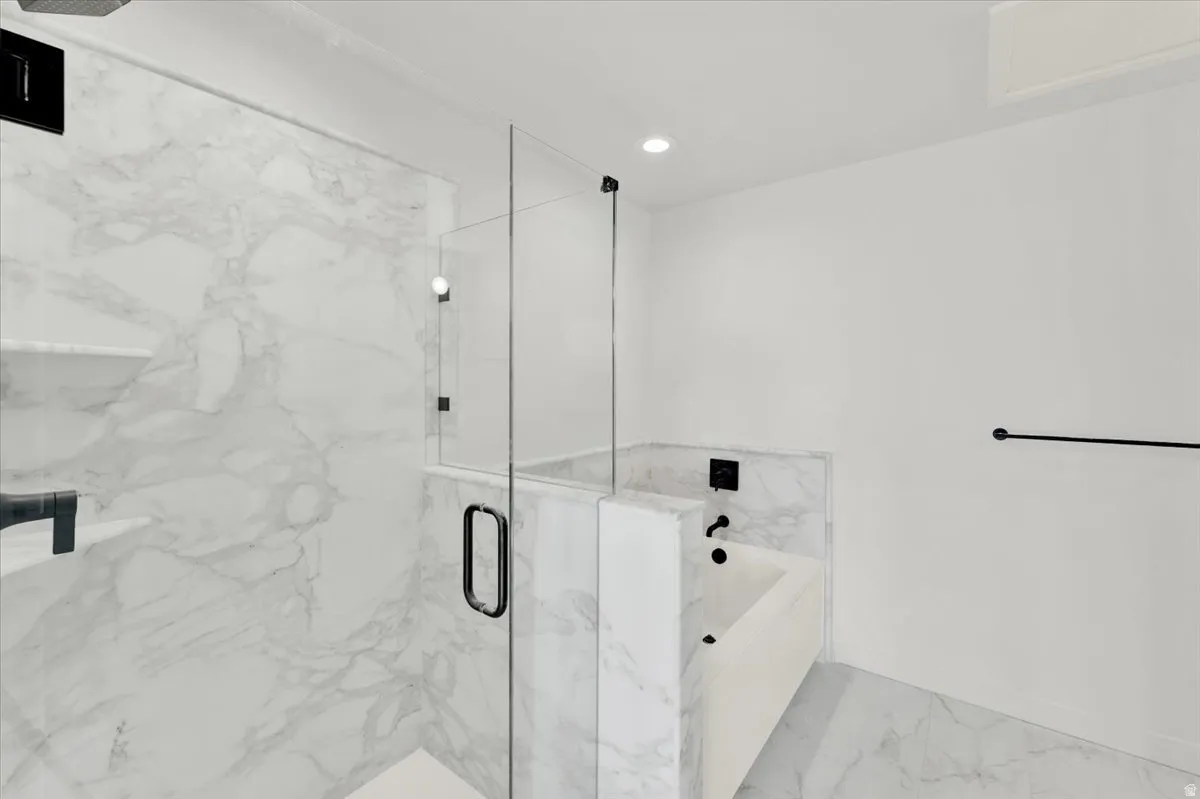 Walk-in shower with clear glass enclosure and black hardware, featuring marble-style tile walls and built-in shelving