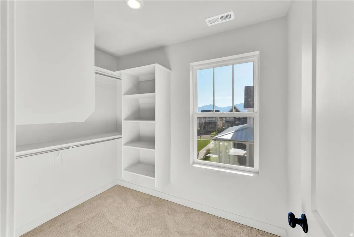 Integrated shelving, built-in hanging rods, recessed ceiling lighting, a single window, and neutral carpeting