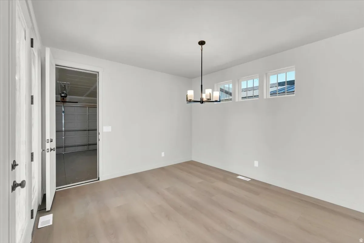 Light wood-finish flooring, three transom windows, and a dark bronze chandelier with five lights