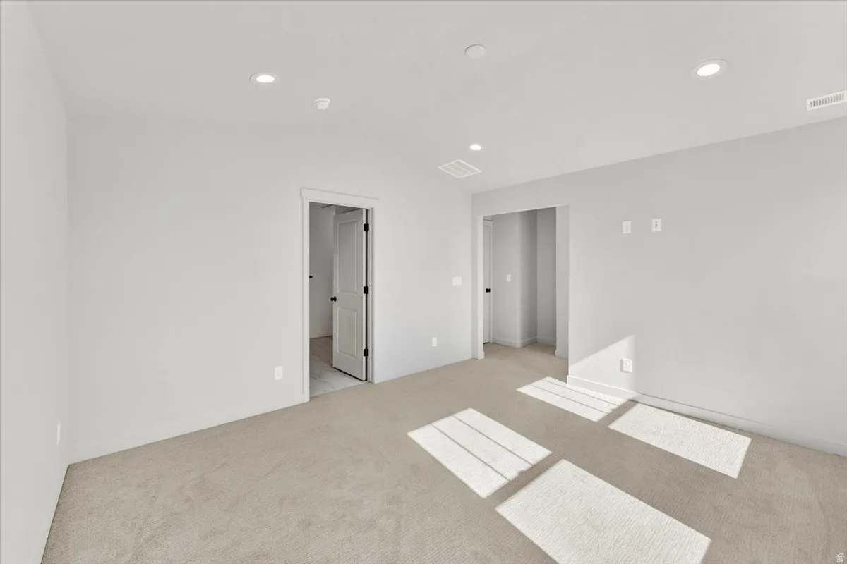 Recessed ceiling lighting illuminates a spacious room featuring neutral-toned carpeting and light gray walls