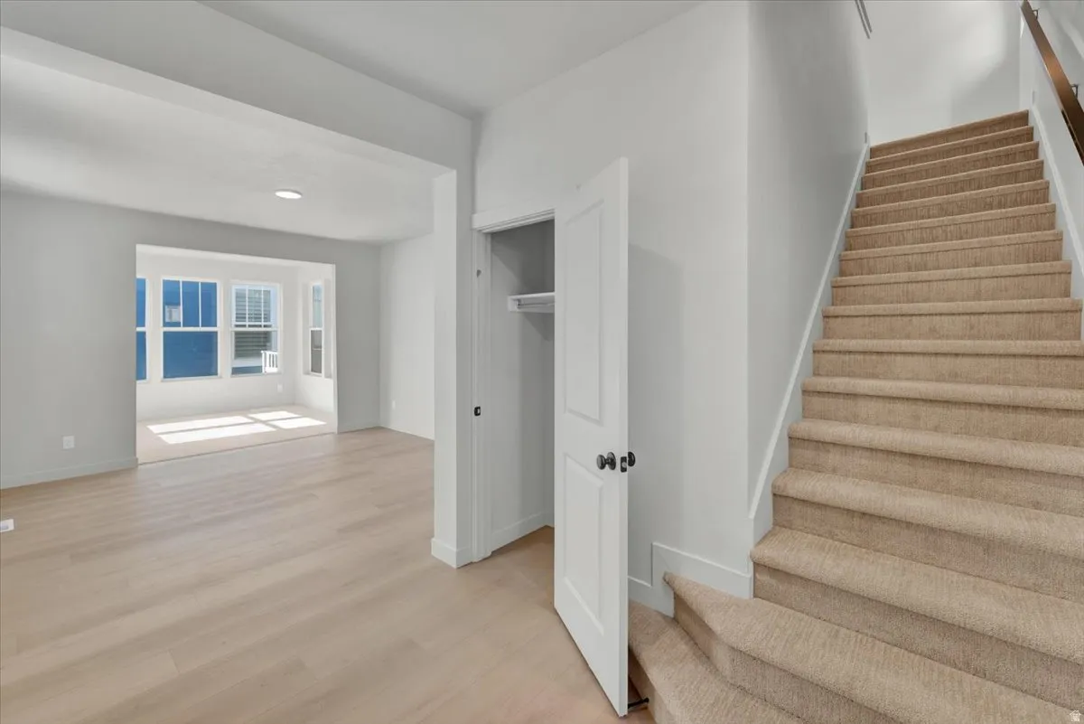 Light wood-finish flooring, recessed lighting, carpeted staircase, paneled interior door, and a multi-pane bay window