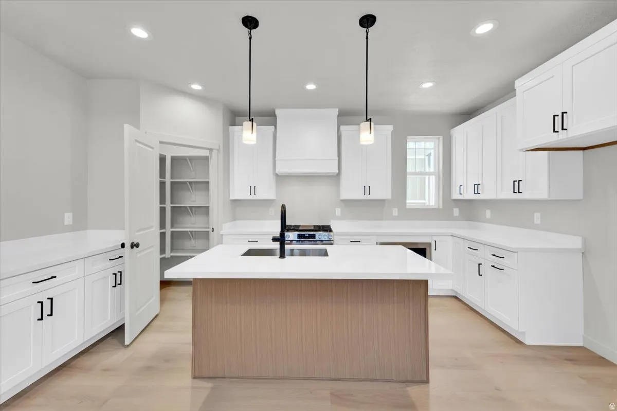 Contemporary kitchen featuring an island with integrated cooktop, white cabinetry, integrated sink, light-toned flooring, and a pantry with shelving