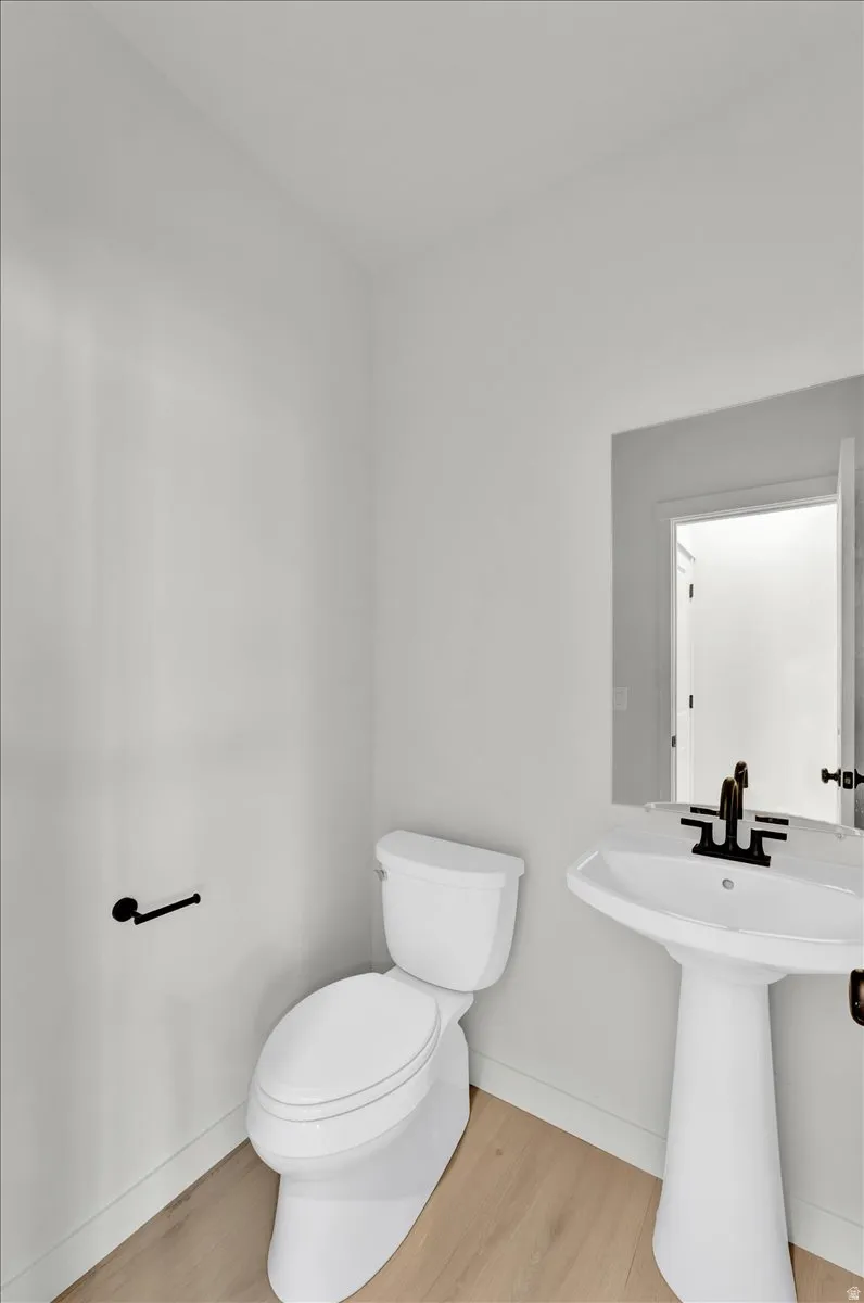 Pedestal sink with a matte black faucet, mirrored vanity, white toilet, and wood-finish flooring