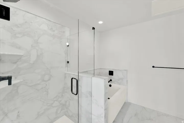 Walk-in shower with clear glass enclosure and black hardware, featuring marble-style tile walls and built-in shelving