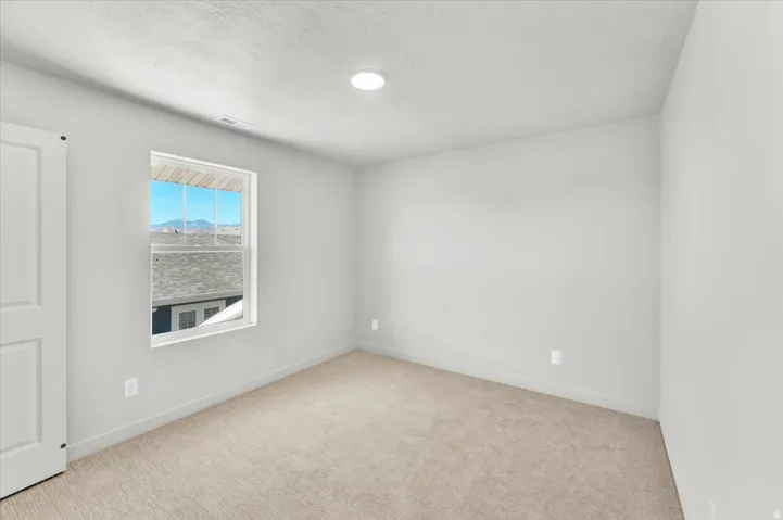 Neutral painted walls, plush carpeting, recessed ceiling lighting, and a white-framed window