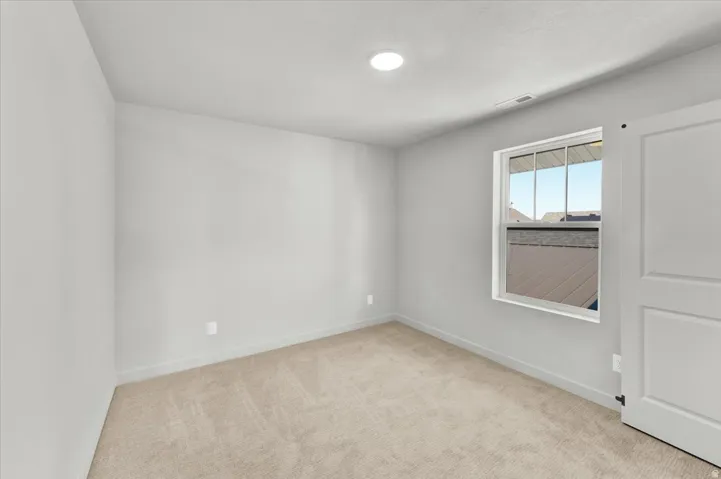 Recessed lighting, light gray wall finish, neutral tone carpet, white trim, and a window with white casing