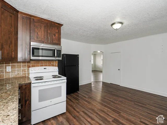 Kitchen featuring dark-toned wood cabinetry, stone-finish countertops, tiled backsplash, and wood-finish flooring