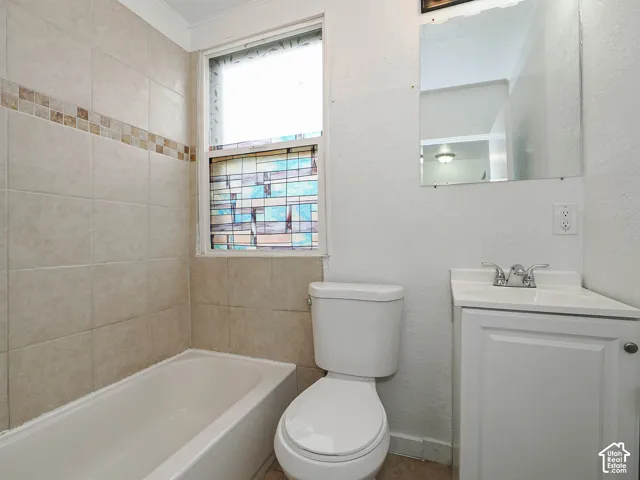 Bathroom featuring a combination bathtub and shower enclosure with neutral-toned wall tiles, decorative mosaic accent border, decorative window insert, white vanity cabinet with a integrated sink, and wall-mounted mirror