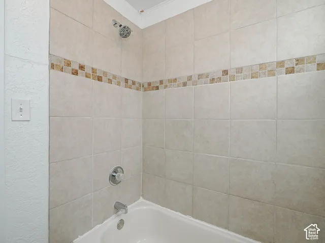 Shower and bathtub combination featuring neutral wall tiles, decorative mosaic tile inlay, chrome fixtures, and a white acrylic tub