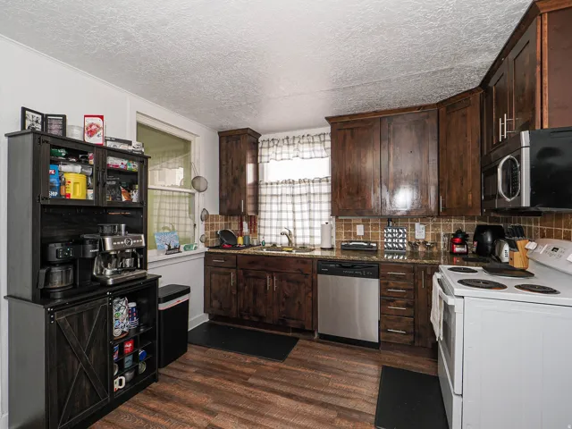 Kitchen featuring wood-finish flooring, dark wood cabinetry, stainless steel dishwasher, white range, and a tiled backsplash