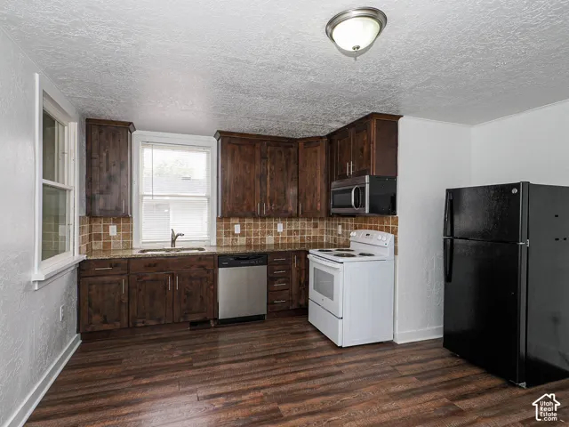 Kitchen featuring dark wood-finish cabinetry, tile backsplash, stone-finish countertops, wood-finish flooring, and stainless steel dishwasher
