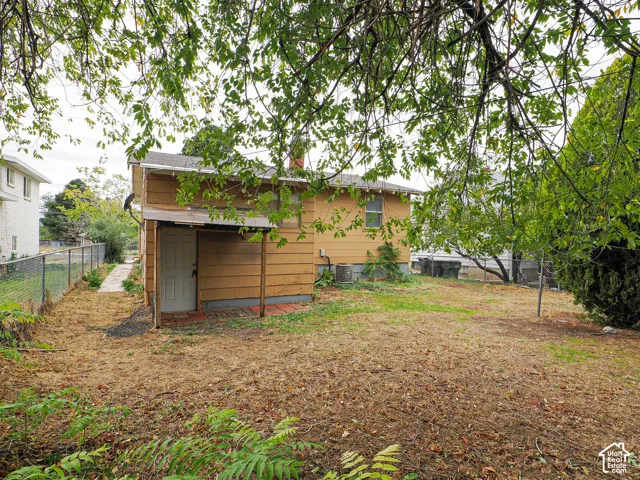 Rear exterior featuring horizontal lap siding, a metal-roofed covered entrance, a masonry chimney, and chain-link perimeter fencing
