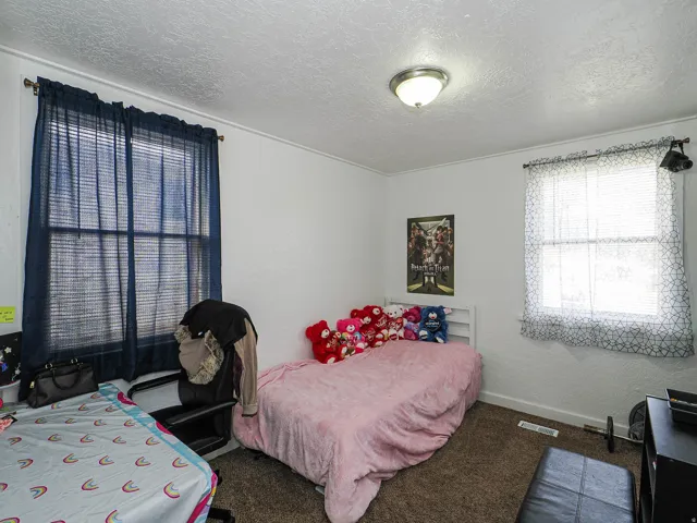 White walls with crown molding, textured ceiling, flush-mount ceiling light fixture, two windows, and dark carpet flooring