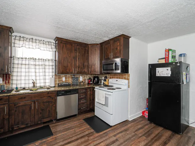 Kitchen featuring wood-finish flooring, dark wood cabinetry, granite-style countertops, and a tile backsplash