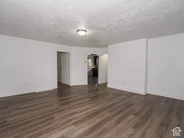 Spacious interior featuring wood-finish flooring, textured ceiling, arched entryway, and flush-mount ceiling lighting