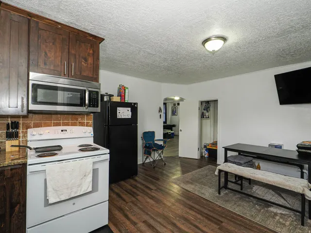 Kitchen featuring wood-finish flooring, dark wood cabinetry, a tiled backsplash, and stainless steel microwave