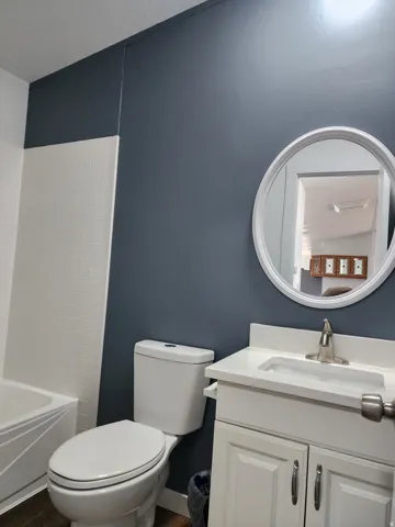 White subway tile wainscoting, a white vanity with a rectangular basin sink, and a circular wall-mounted mirror