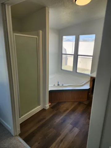 Walk-in shower with frosted glass enclosure, built-in corner bathtub, wood-finish flooring, and recessed lighting