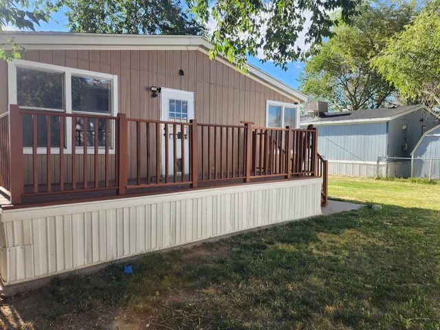 Exterior featuring brown siding, white trim, a brown wooden deck with matching railings, and a white entry door with glass inserts
