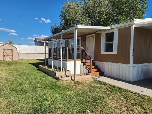 Brown exterior siding with white trim, covered porch with dark railings, wood stairs, separate storage shed, and a concrete walkway