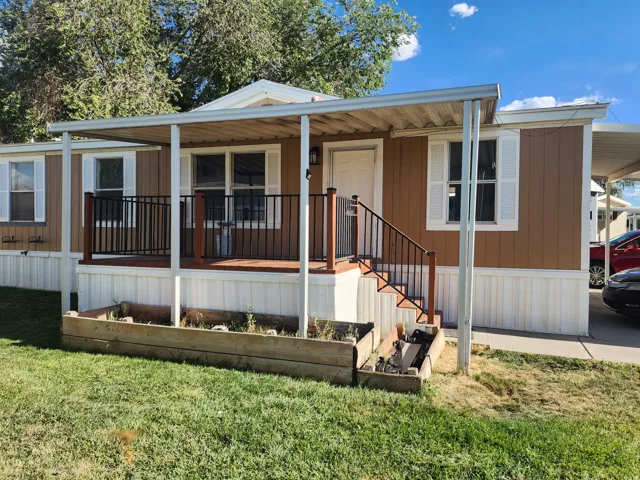 Covered front porch with black metal railings, white exterior shutters, and a carport