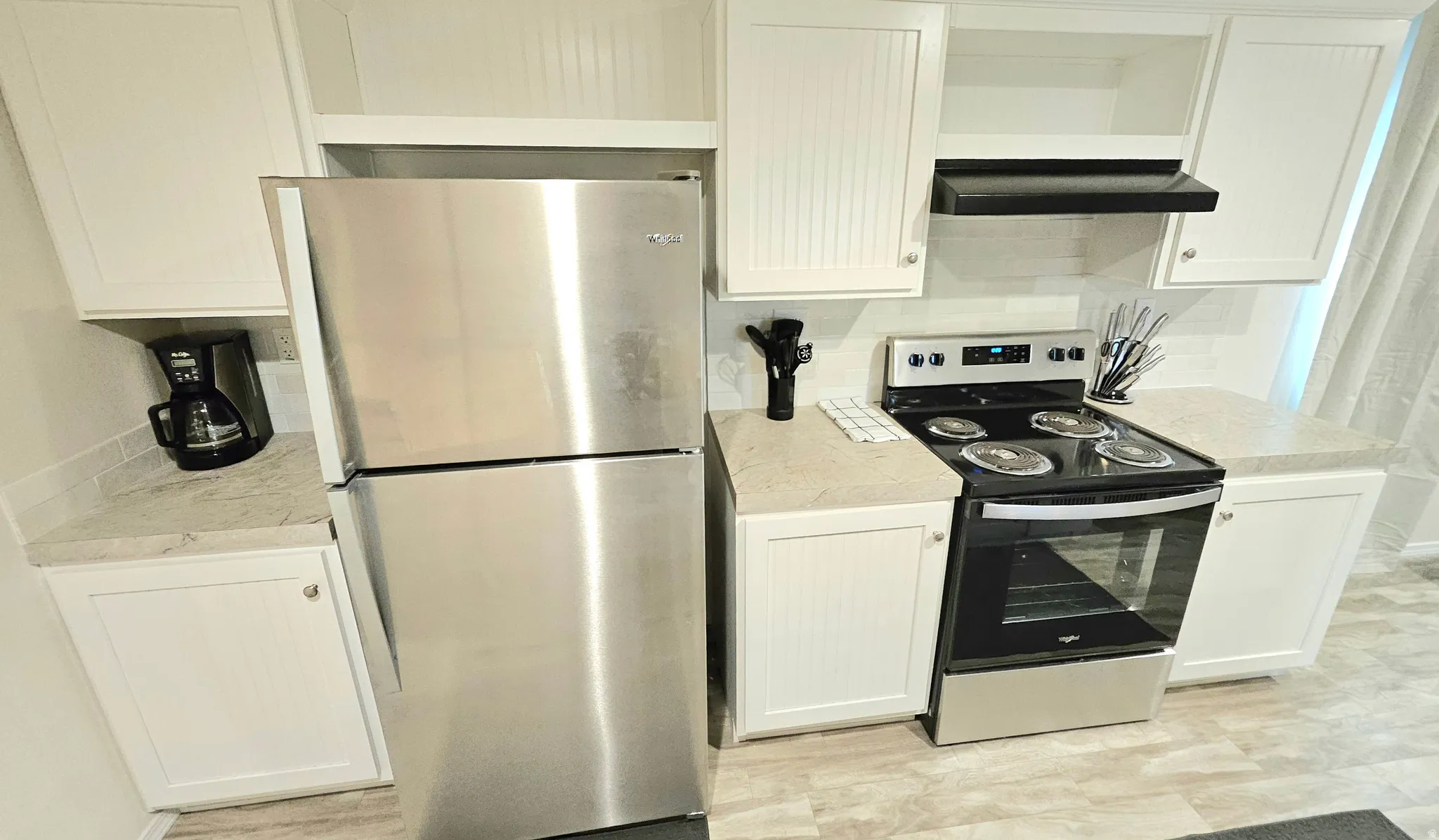 Kitchen featuring white cabinetry, stainless steel appliances, light-toned countertops, and a white tile backsplash