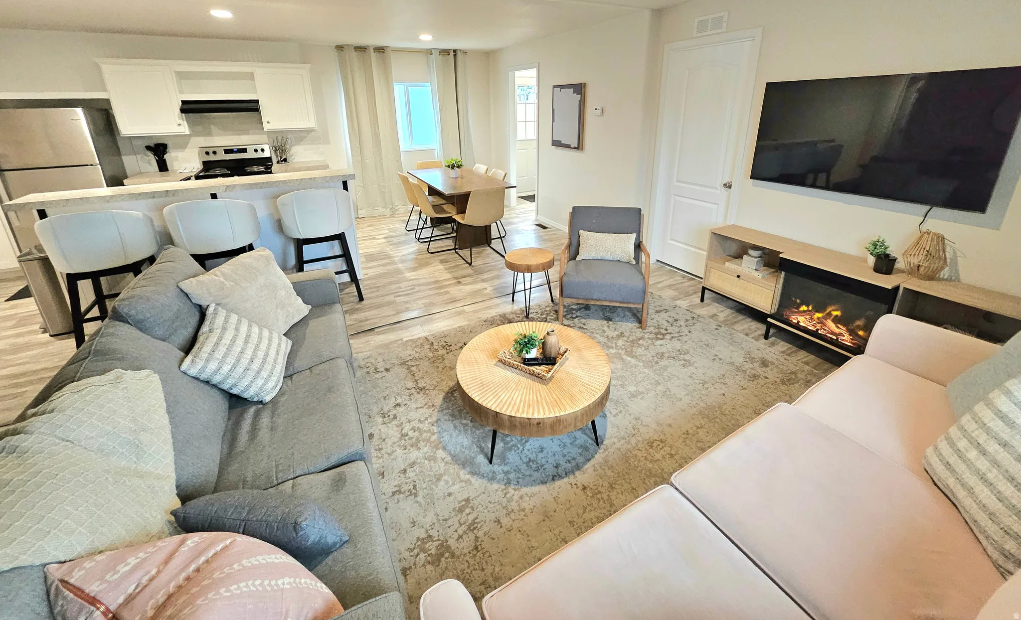 Open-concept living space featuring wood-finish flooring, white cabinetry, integrated range with overhead ventilation, and a built-in media console with a fireplace insert