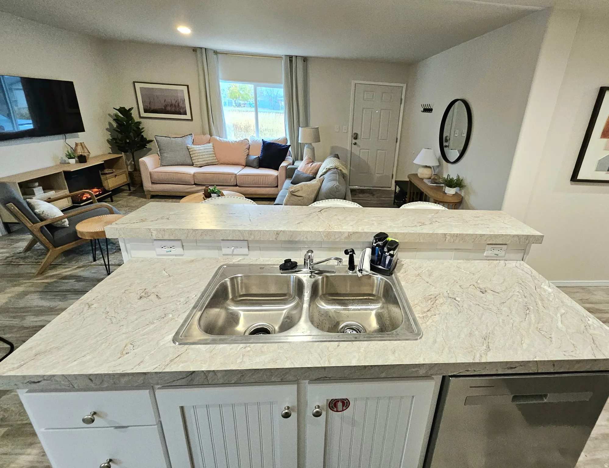 Kitchen island with a double basin stainless steel sink, light-toned countertops, and white cabinetry