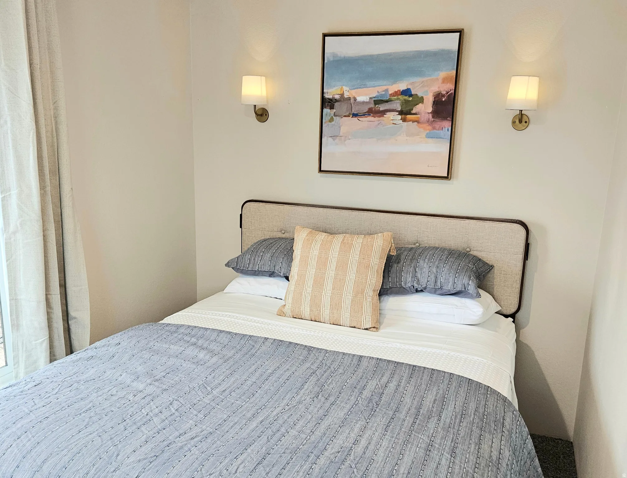 Upholstered headboard with an integrated frame, wall-mounted sconce lighting, and light-toned wall finishes