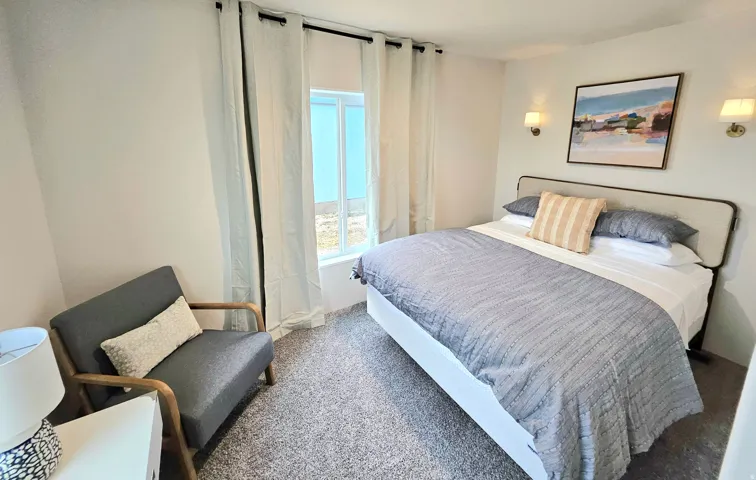 Window with white curtains, wall-mounted sconce lighting, and gray carpet flooring