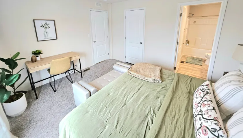 Carpeted bedroom featuring white paneled doors and a full bathroom with a white bathtub