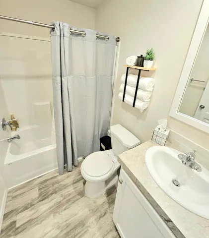 Wood-finish flooring, white vanity with integrated sink, light-toned countertop, shower-over-tub combination, and wall-mounted shelving