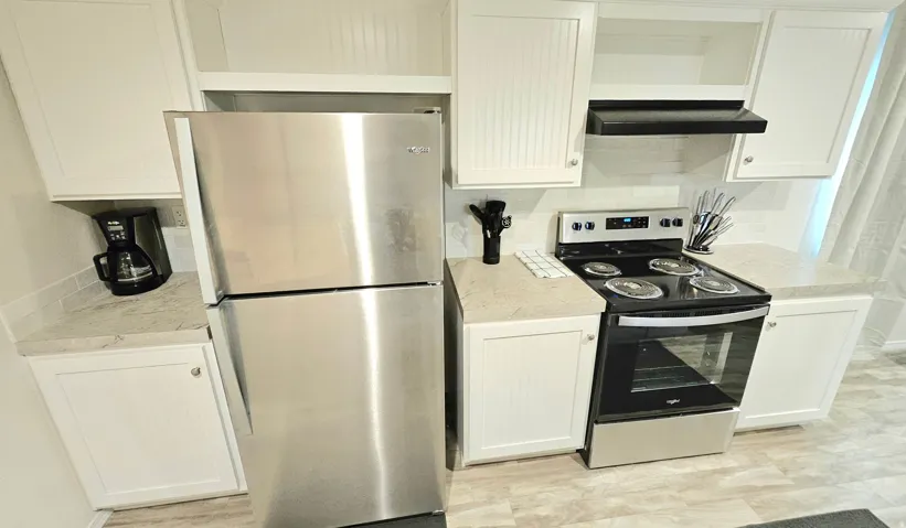 Kitchen featuring white cabinetry, stainless steel appliances, light-toned countertops, and a white tile backsplash