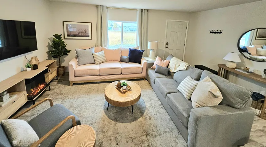 Spacious living area featuring light wood-finish flooring, a contemporary built-in electric fireplace, and abundant natural light from a large window