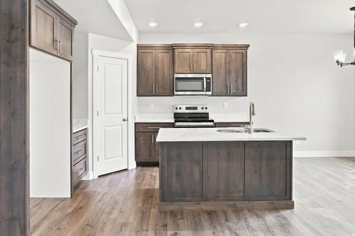 Kitchen with wood-finish flooring, dark wood cabinetry, white countertops, stainless steel microwave, and integrated sink