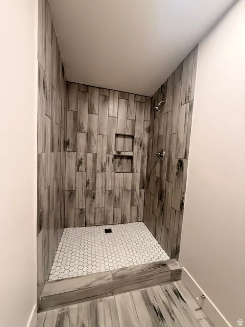 Walk-in shower featuring wood-look tile, a built-in shower niche, hexagonal tile shower pan, and a chrome shower fixture