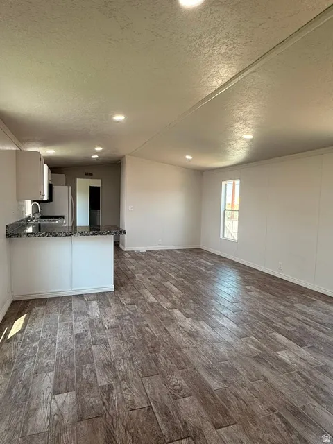 Expansive living area with wood-finish flooring, recessed lighting, and a kitchen featuring white cabinetry and dark countertops