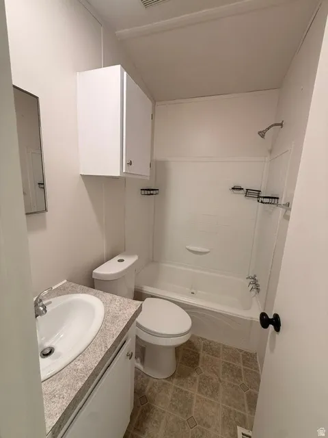 White vanity with integrated sink, speckled countertop, white built-in cabinetry, full bathtub with shower, and patterned floor tile