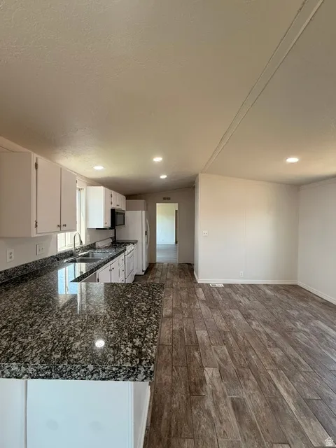 Kitchen featuring white cabinetry, dark speckled countertops, stainless-steel sink, and recessed lighting