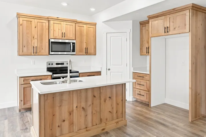 Kitchen featuring natural wood-finish cabinetry, stainless steel microwave, white countertops, and a central island with an integrated sink