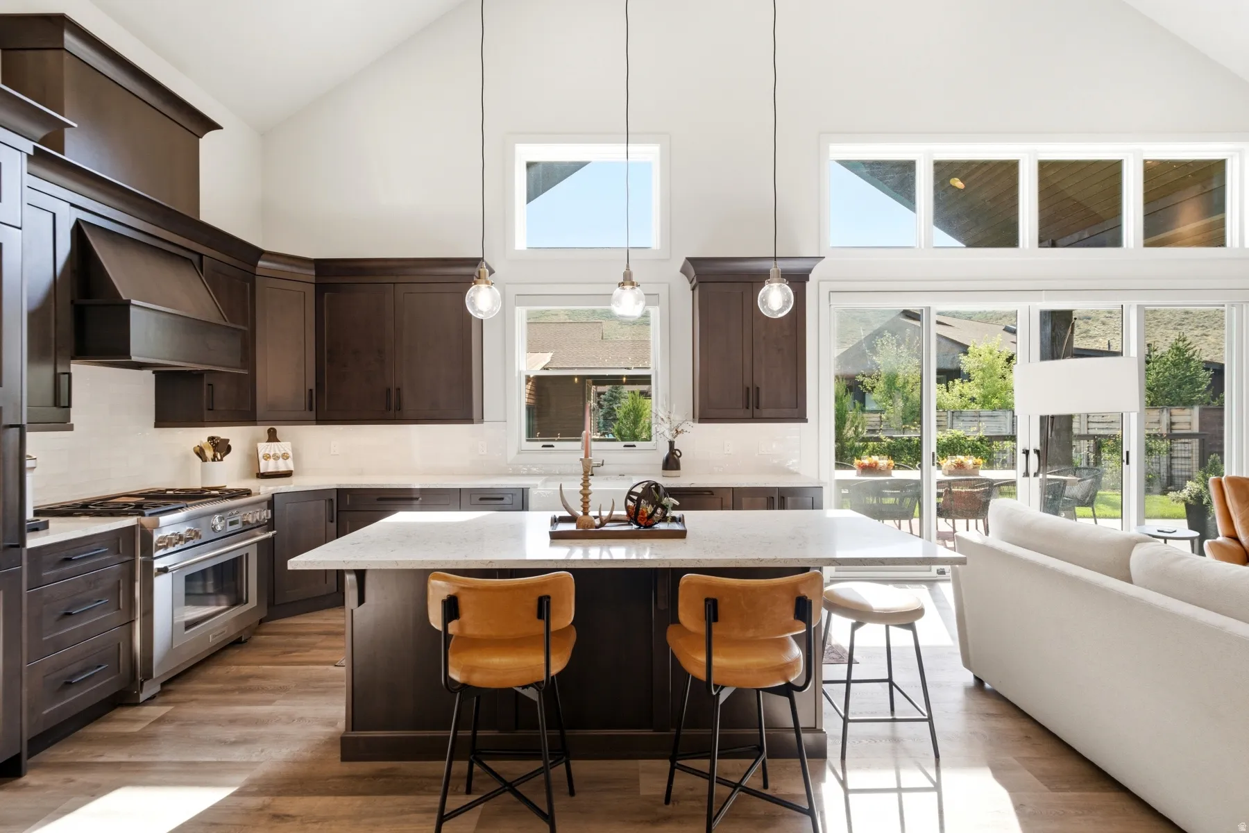 Vaulted ceiling with abundant natural light, dark wood-finish cabinetry, stainless steel range, light-toned countertops, and wood-finish flooring