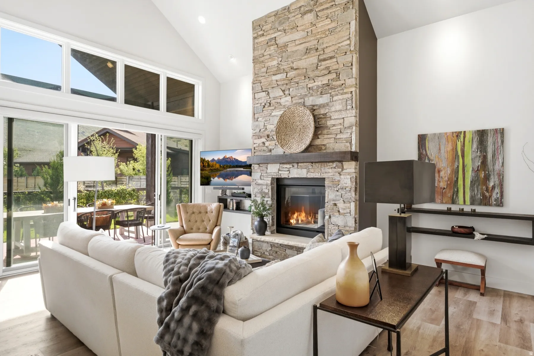 Vaulted ceiling, stone-clad fireplace with mantel, wood-finish flooring, and expansive glass sliding doors