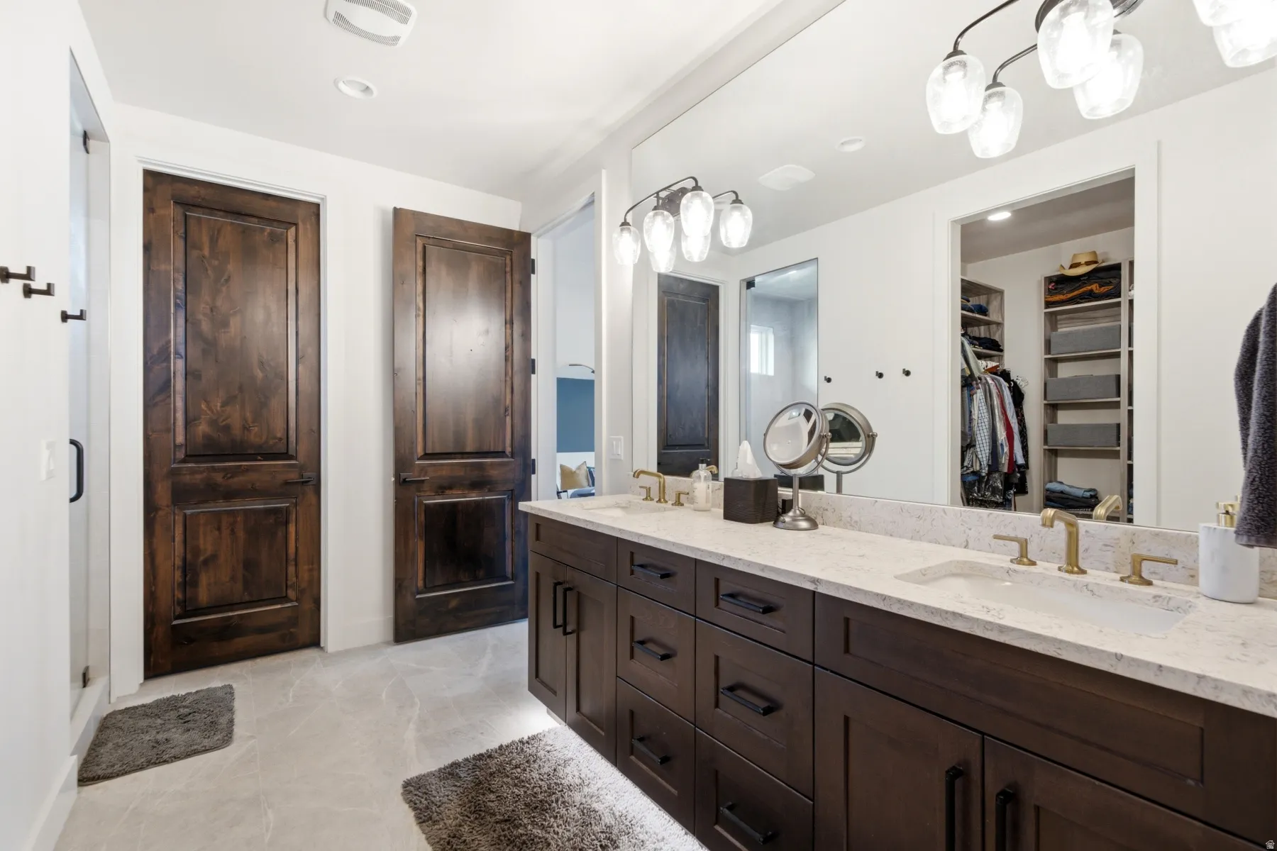 Dual vanity with dark wood-finish cabinetry, light stone countertop, and brass-finish fixtures