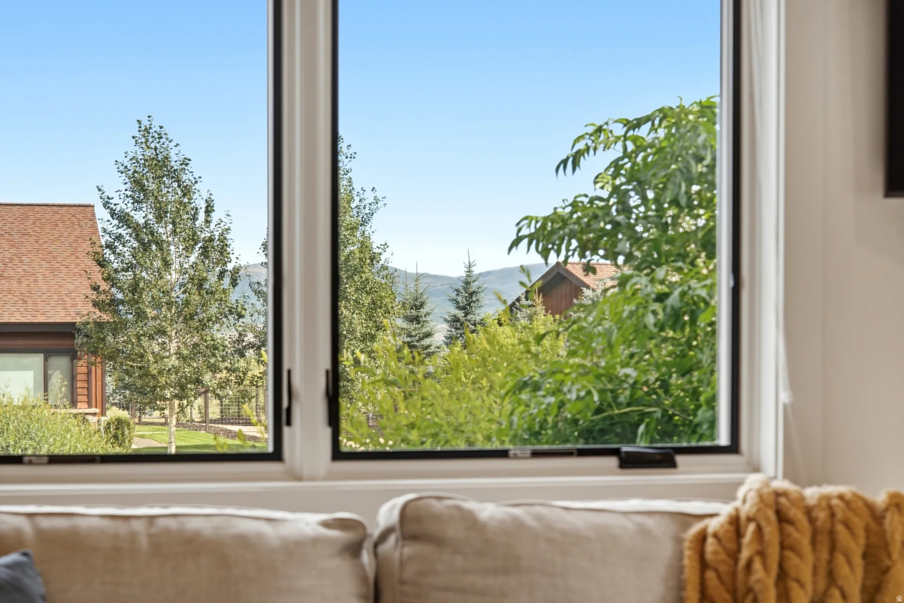 White-framed window with black hardware overlooking a natural landscape with distant mountains