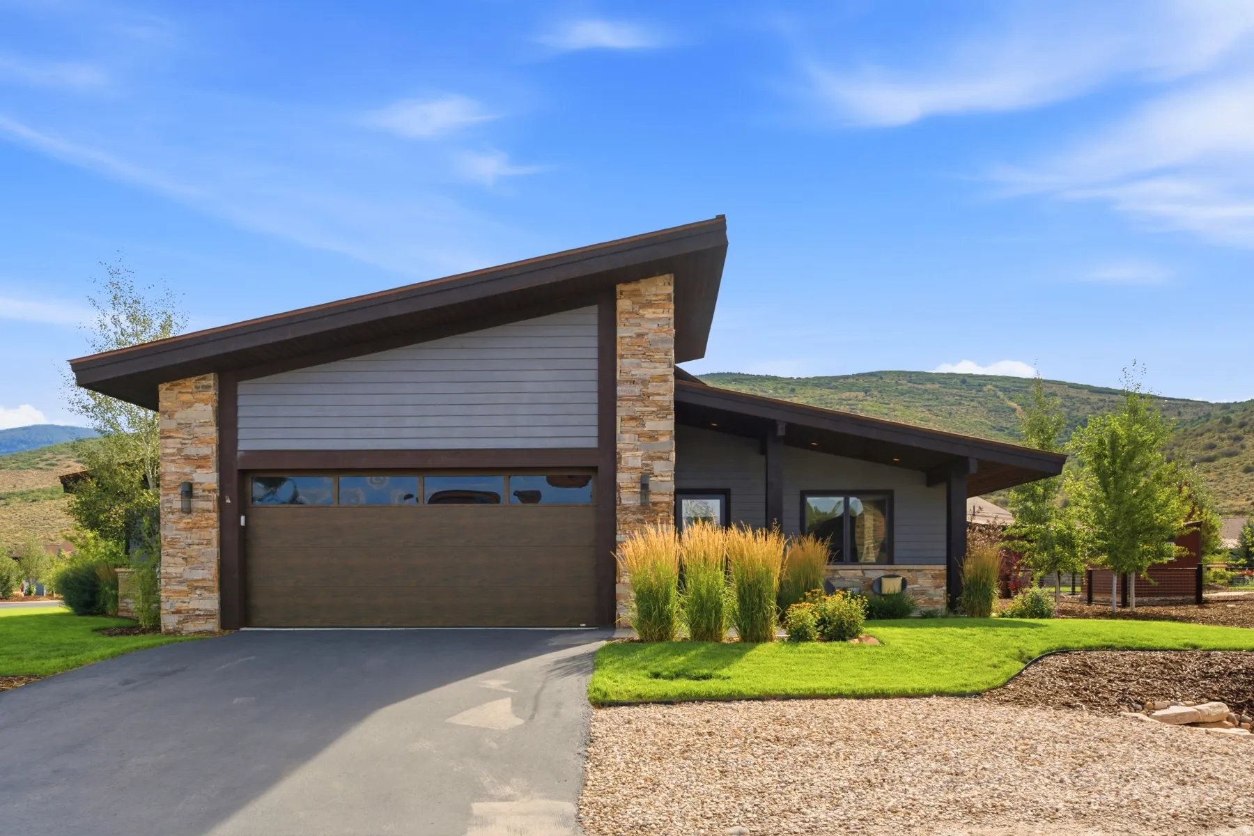 Contemporary exterior featuring a low-slope roofline, stone veneer accents, horizontal siding, and a modern garage door with windows