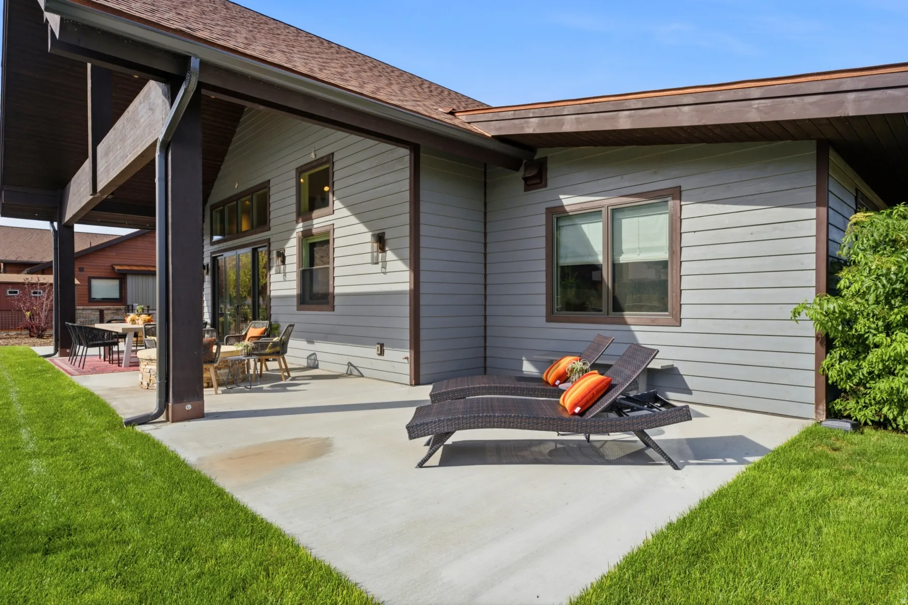 Expansive concrete patio with a covered outdoor entertaining area, featuring large sliding glass doors, a gabled roofline, and gray siding with brown trim